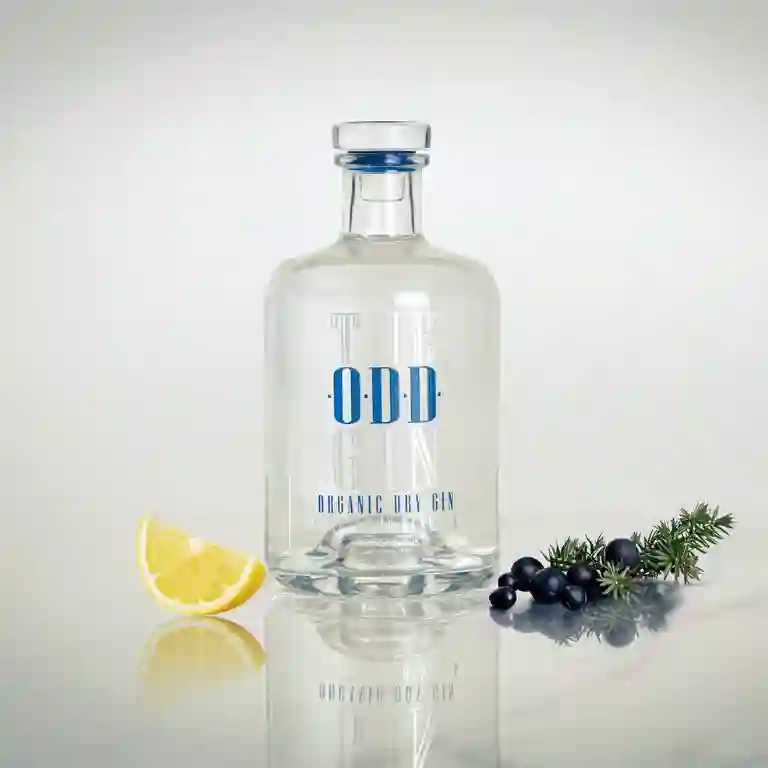 The ODD Gin med en ginflaske – Organic Dry - placeret ved siden af enebærgren og citronskive i et lyst marmor lignende setup