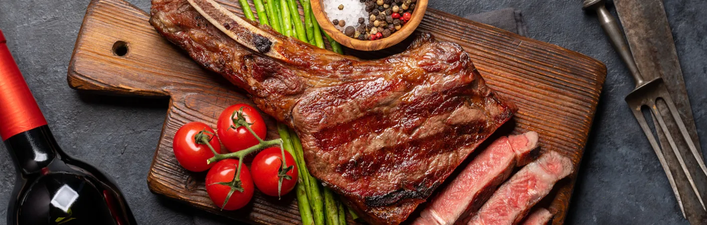 Grillet steak på træskærebræt med asparges, cherrytomater, krydderier og rødvin, der illustrerer vine, som passer til kødretter