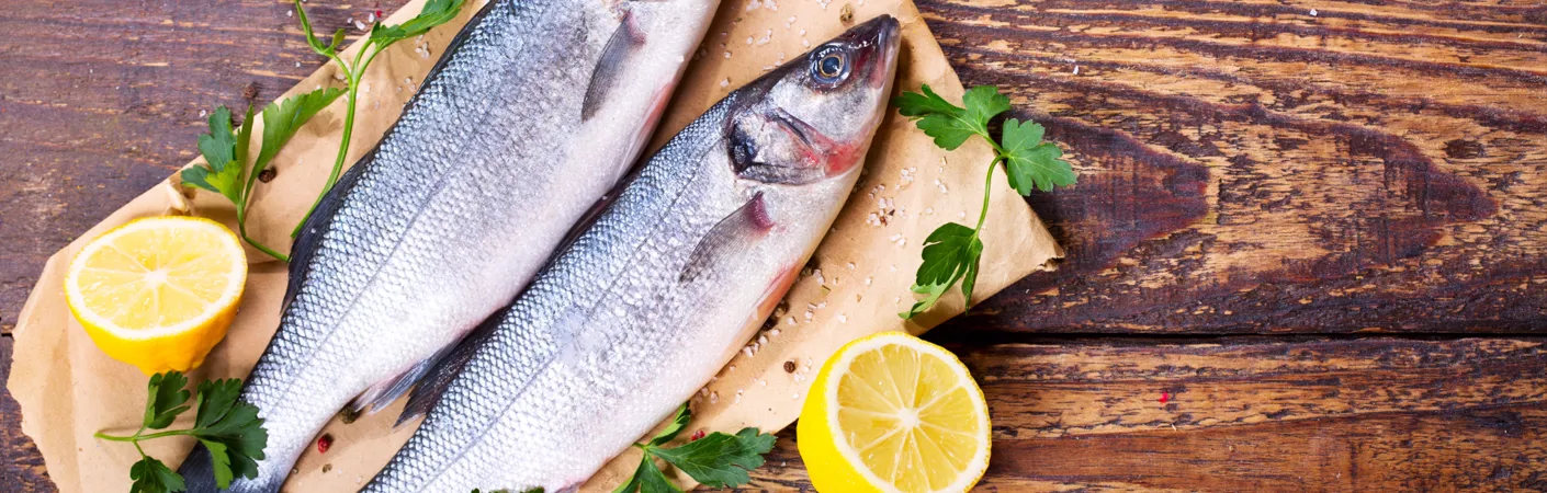 Friske hele fisk anrettet på træbord med citron og krydderurter, som illustrerer vine, der passer til fiskeretter